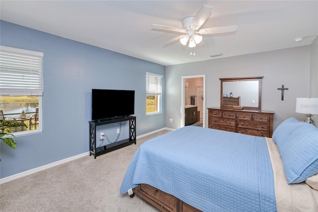 bedroom with ensuite bathroom, light colored carpet, and ceiling fan