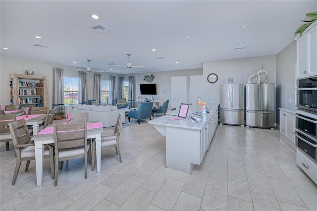 kitchen featuring white cabinetry, light stone counters, a kitchen island with sink, and stainless steel fridge