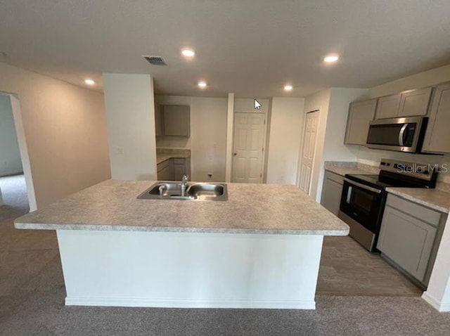 kitchen with sink, gray cabinets, appliances with stainless steel finishes, carpet, and a center island with sink