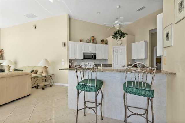 kitchen featuring dark stone countertops, light tile patterned floors, a kitchen breakfast bar, kitchen peninsula, and white cabinets