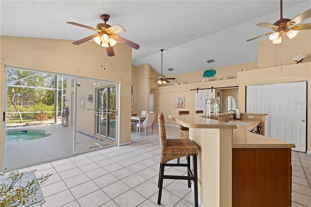 kitchen with a kitchen bar, sink, high vaulted ceiling, a textured ceiling, and light tile patterned floors