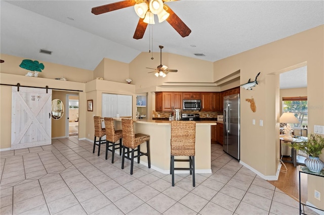 kitchen with a breakfast bar, backsplash, kitchen peninsula, stainless steel appliances, and a barn door