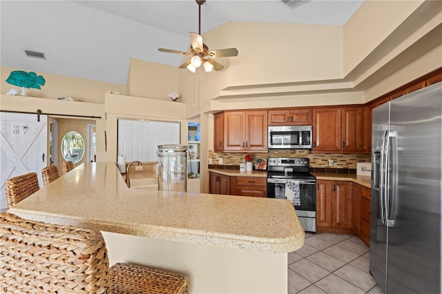 kitchen with a barn door, stainless steel appliances, a kitchen breakfast bar, and tasteful backsplash