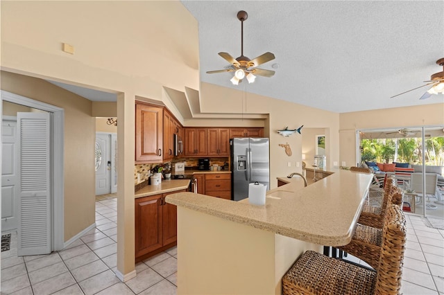 kitchen with light tile patterned flooring, backsplash, a kitchen breakfast bar, ceiling fan, and stainless steel appliances