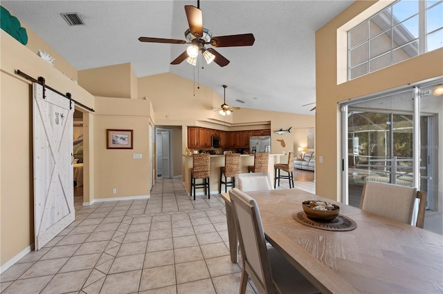 tiled dining space with ceiling fan, a barn door, high vaulted ceiling, and a textured ceiling