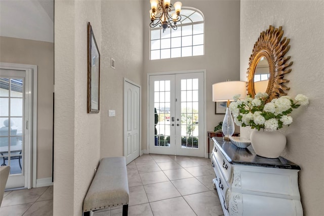 entryway with an inviting chandelier, light tile patterned floors, a towering ceiling, and french doors