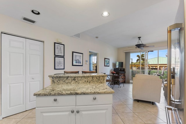 kitchen featuring light tile patterned floors, ceiling fan, a center island, light stone counters, and white cabinets