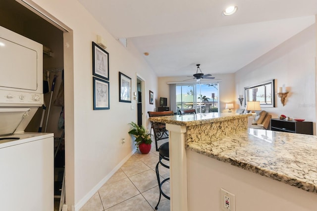 kitchen with a breakfast bar, light stone counters, light tile patterned floors, ceiling fan, and stacked washing maching and dryer