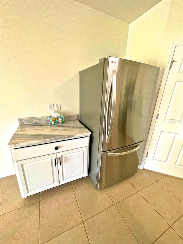 kitchen with butcher block countertops, light tile patterned floors, white cabinets, and stainless steel refrigerator