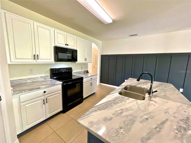 kitchen with sink, light tile patterned floors, a kitchen island with sink, black appliances, and white cabinets