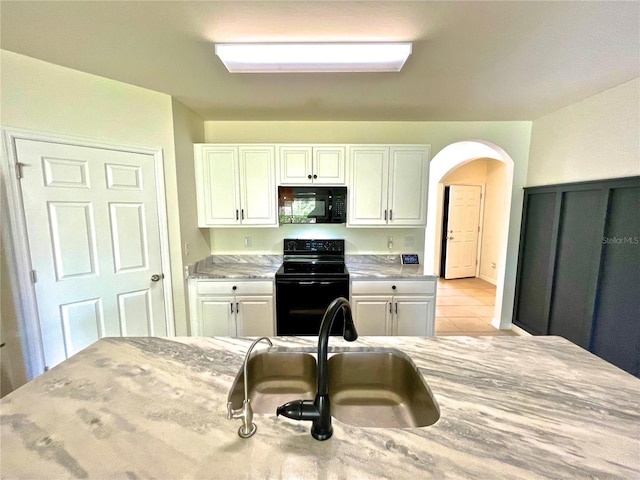 kitchen with sink, light tile patterned floors, white cabinets, and black appliances