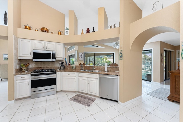 kitchen featuring sink, white cabinetry, light tile patterned floors, dark stone countertops, and appliances with stainless steel finishes