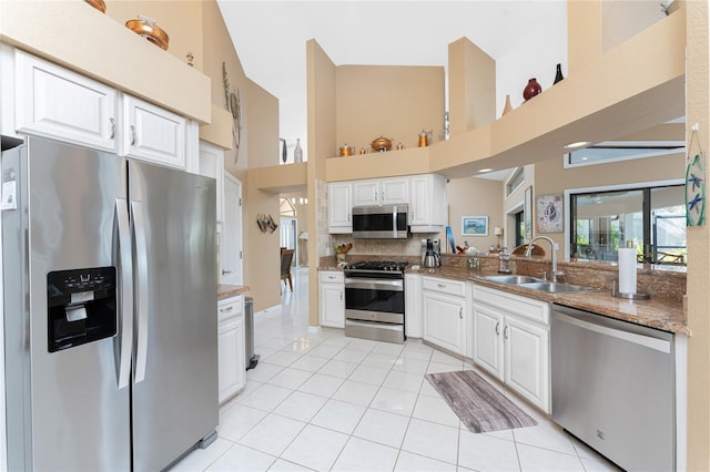 kitchen with sink, light tile patterned floors, appliances with stainless steel finishes, a towering ceiling, and white cabinets