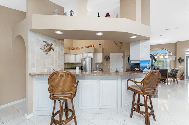 kitchen with a breakfast bar area, kitchen peninsula, white cabinets, and stainless steel refrigerator with ice dispenser