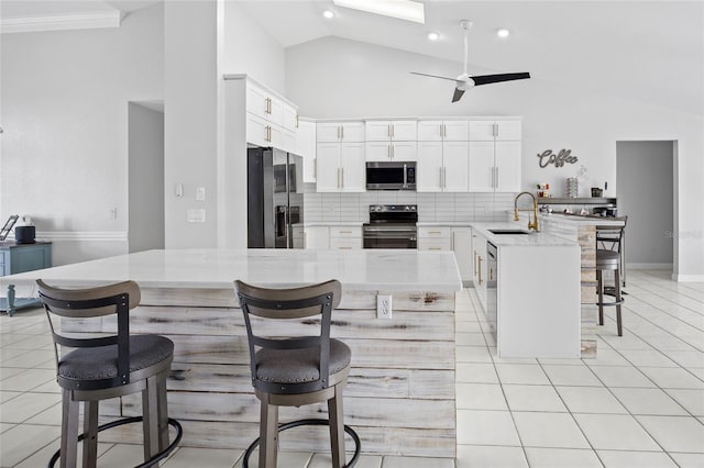 kitchen featuring light tile patterned flooring, appliances with stainless steel finishes, sink, white cabinets, and a kitchen bar