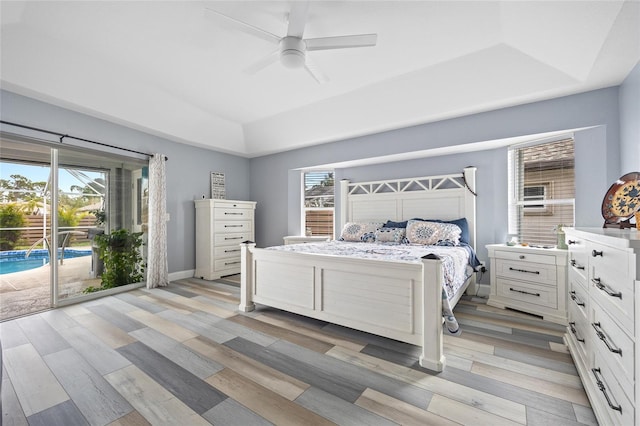 bedroom featuring a tray ceiling, light wood-type flooring, multiple windows, and access to outside