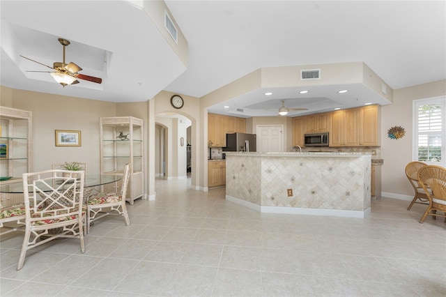 kitchen with ceiling fan, stainless steel appliances, a tray ceiling, light tile patterned flooring, and light brown cabinetry