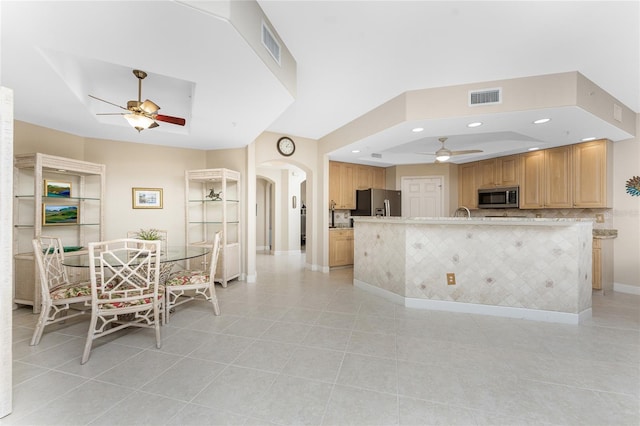 kitchen with ceiling fan, stainless steel appliances, a tray ceiling, and light tile patterned floors