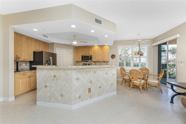 kitchen with stainless steel appliances, an island with sink, a raised ceiling, and decorative light fixtures