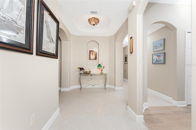 hallway with a tray ceiling and light tile patterned floors