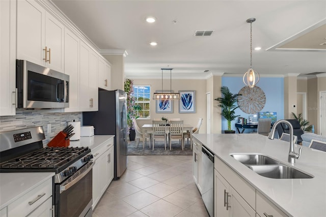 kitchen with sink, crown molding, appliances with stainless steel finishes, white cabinetry, and hanging light fixtures