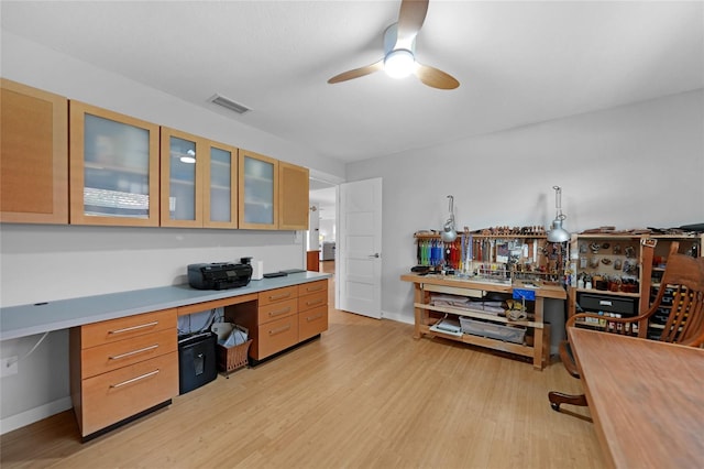 home office featuring ceiling fan, built in desk, and light hardwood / wood-style flooring