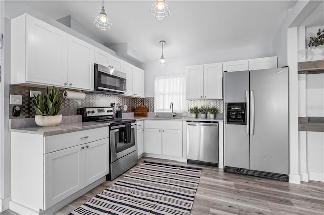 kitchen with vaulted ceiling, pendant lighting, white cabinetry, sink, and stainless steel appliances