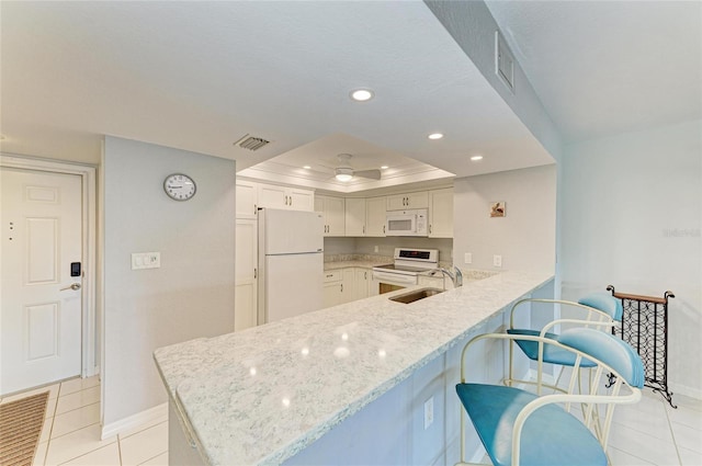 kitchen featuring sink, white appliances, white cabinetry, a tray ceiling, and kitchen peninsula