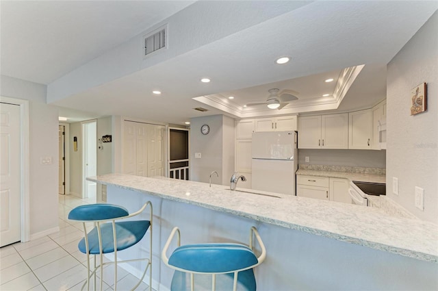 kitchen with white appliances, a breakfast bar, a tray ceiling, white cabinets, and kitchen peninsula