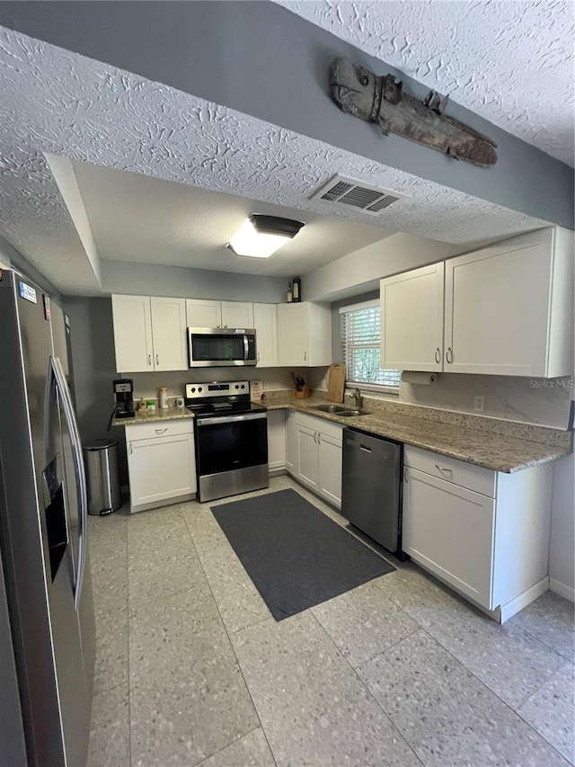 kitchen featuring stainless steel appliances, white cabinetry, sink, and a textured ceiling