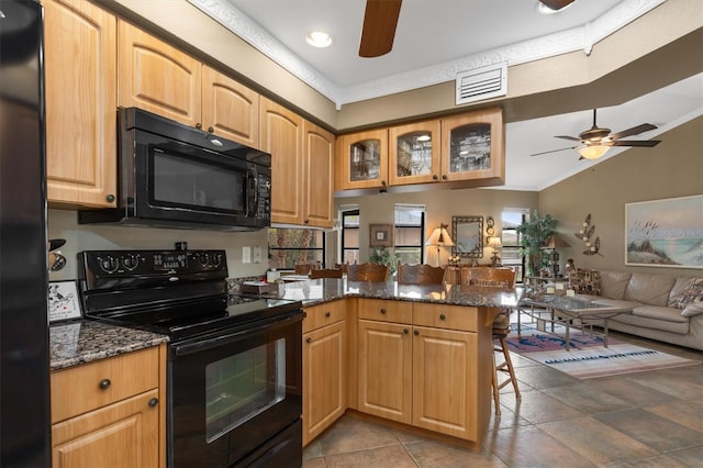 kitchen featuring dark stone countertops, a kitchen bar, kitchen peninsula, and black appliances