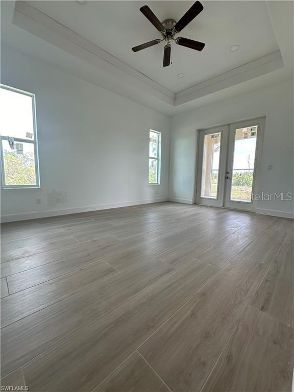 spare room featuring ceiling fan, a raised ceiling, light wood-type flooring, and a wealth of natural light