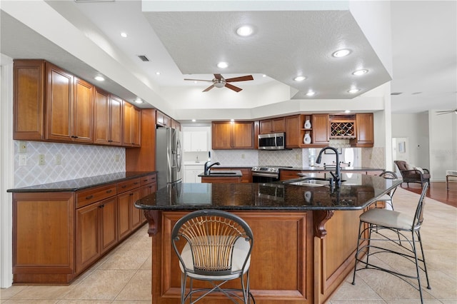 kitchen featuring sink, ceiling fan, dark stone countertops, stainless steel appliances, and a kitchen bar