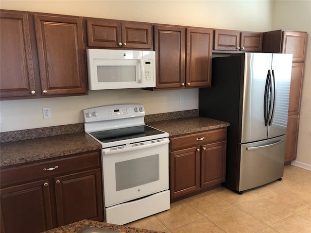 kitchen with dark brown cabinets, light tile patterned floors, and white appliances