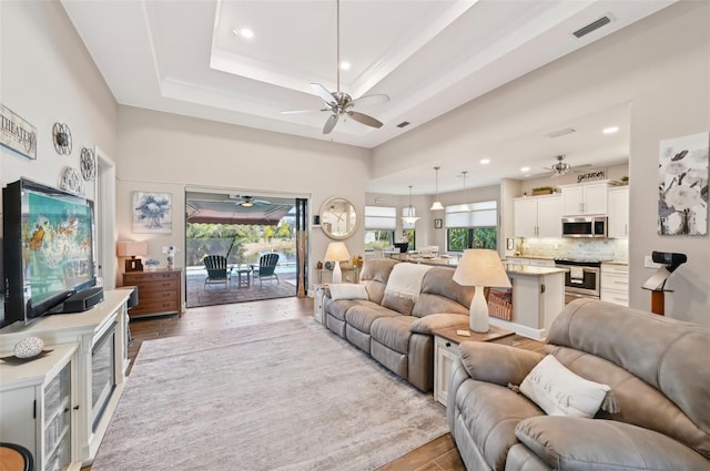 living room featuring ceiling fan, a raised ceiling, and light wood-type flooring