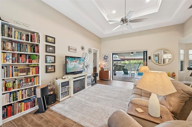 living room featuring a high ceiling, wood-type flooring, a raised ceiling, and ceiling fan