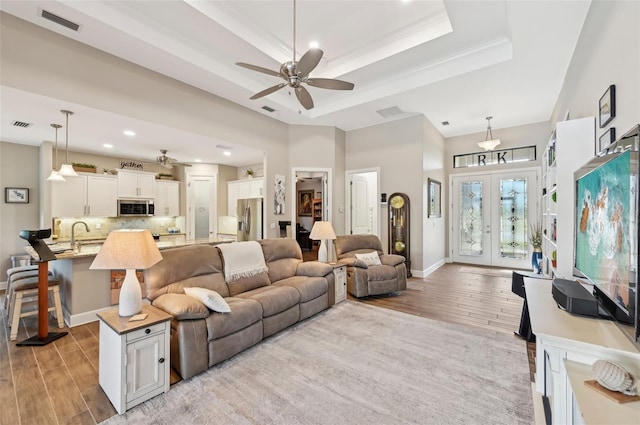 living room featuring french doors, light hardwood / wood-style flooring, a raised ceiling, ceiling fan, and a high ceiling