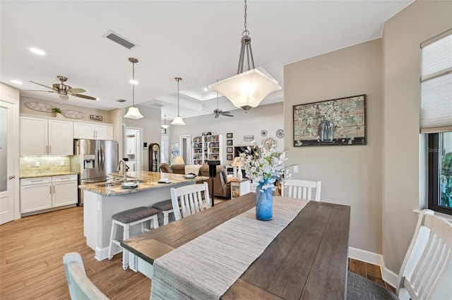 dining room with ceiling fan, a raised ceiling, and light hardwood / wood-style floors