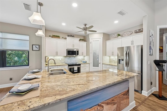 kitchen with sink, white cabinetry, hanging light fixtures, appliances with stainless steel finishes, and decorative backsplash