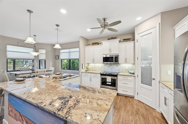 kitchen featuring appliances with stainless steel finishes, sink, white cabinets, hanging light fixtures, and a center island with sink