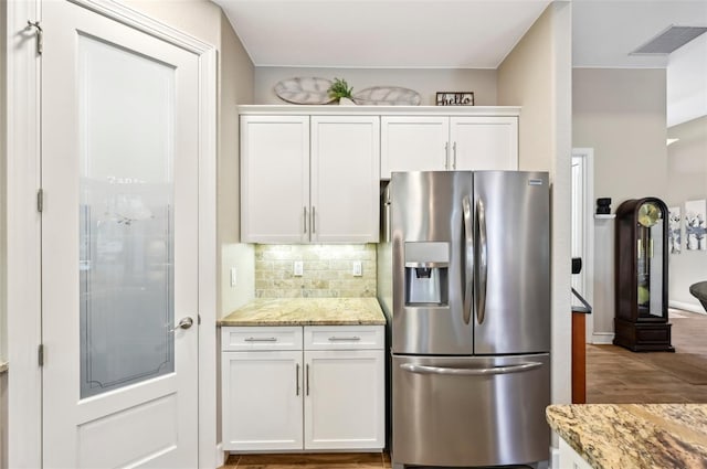 kitchen with white cabinetry, light stone countertops, stainless steel fridge with ice dispenser, and decorative backsplash