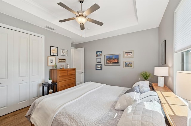 bedroom featuring a closet, hardwood / wood-style floors, a raised ceiling, and ceiling fan