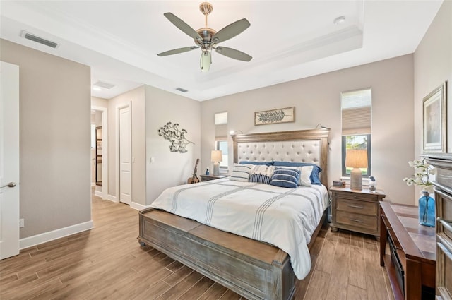 bedroom with ceiling fan, a tray ceiling, and light hardwood / wood-style flooring