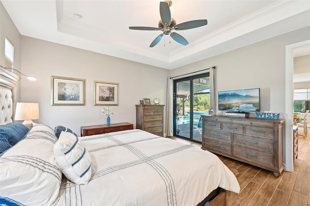 bedroom with wood-type flooring, access to exterior, ceiling fan, and a tray ceiling