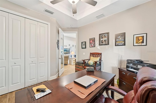 home office featuring a raised ceiling, crown molding, ceiling fan, and light hardwood / wood-style floors