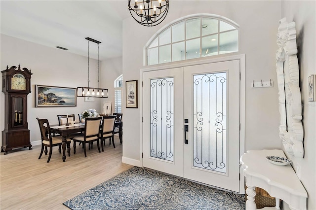 foyer featuring french doors, a chandelier, a high ceiling, and light wood-type flooring