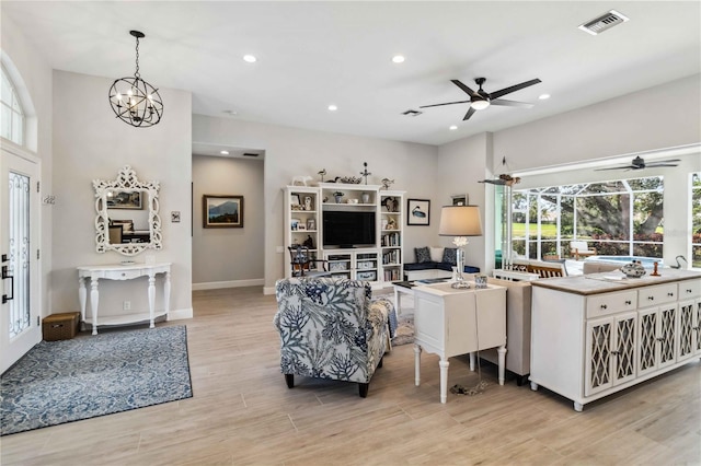 living room featuring ceiling fan with notable chandelier and light hardwood / wood-style flooring