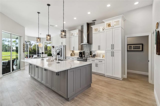 kitchen with decorative light fixtures, sink, white cabinets, a kitchen island with sink, and wall chimney exhaust hood