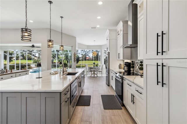 kitchen with a large island, wall chimney range hood, sink, appliances with stainless steel finishes, and hanging light fixtures