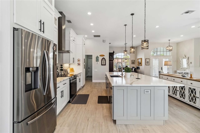 kitchen with wall chimney range hood, appliances with stainless steel finishes, hanging light fixtures, a spacious island, and white cabinets